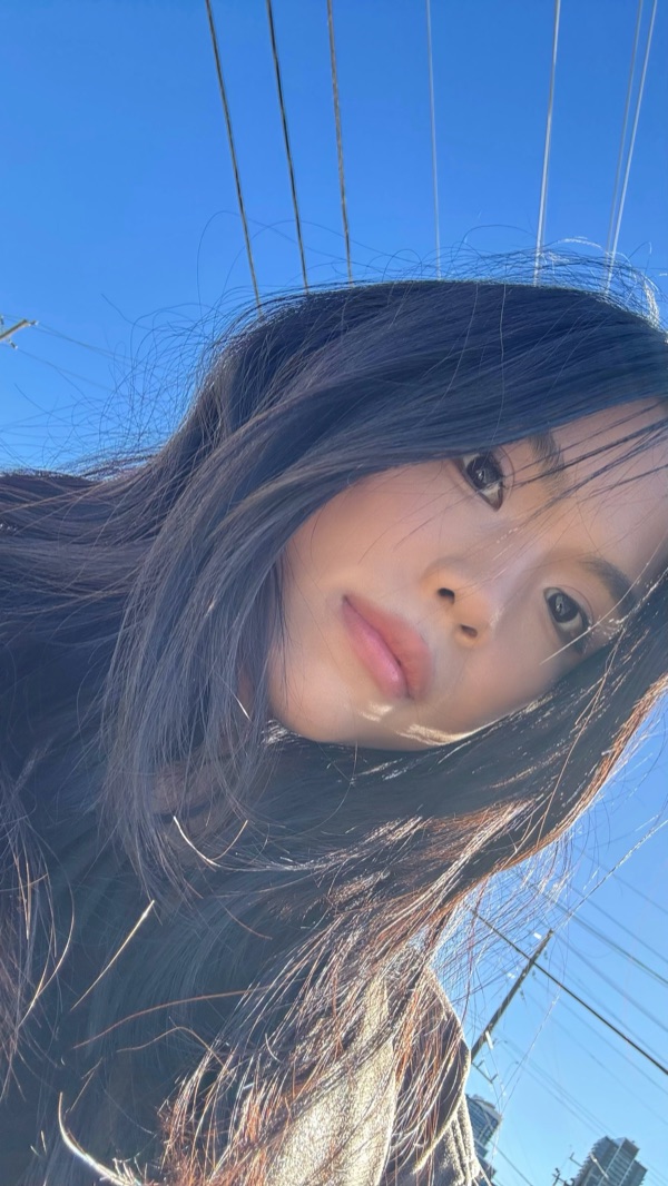 Selfie of Zeaj from below, long dark hair blowing against a clear blue sky